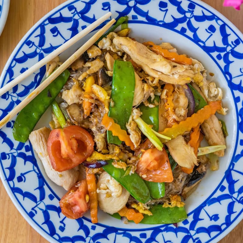 Stir-fried chicken, vegetables, and glass noodles on a blue and white patterned plate with chopsticks.
